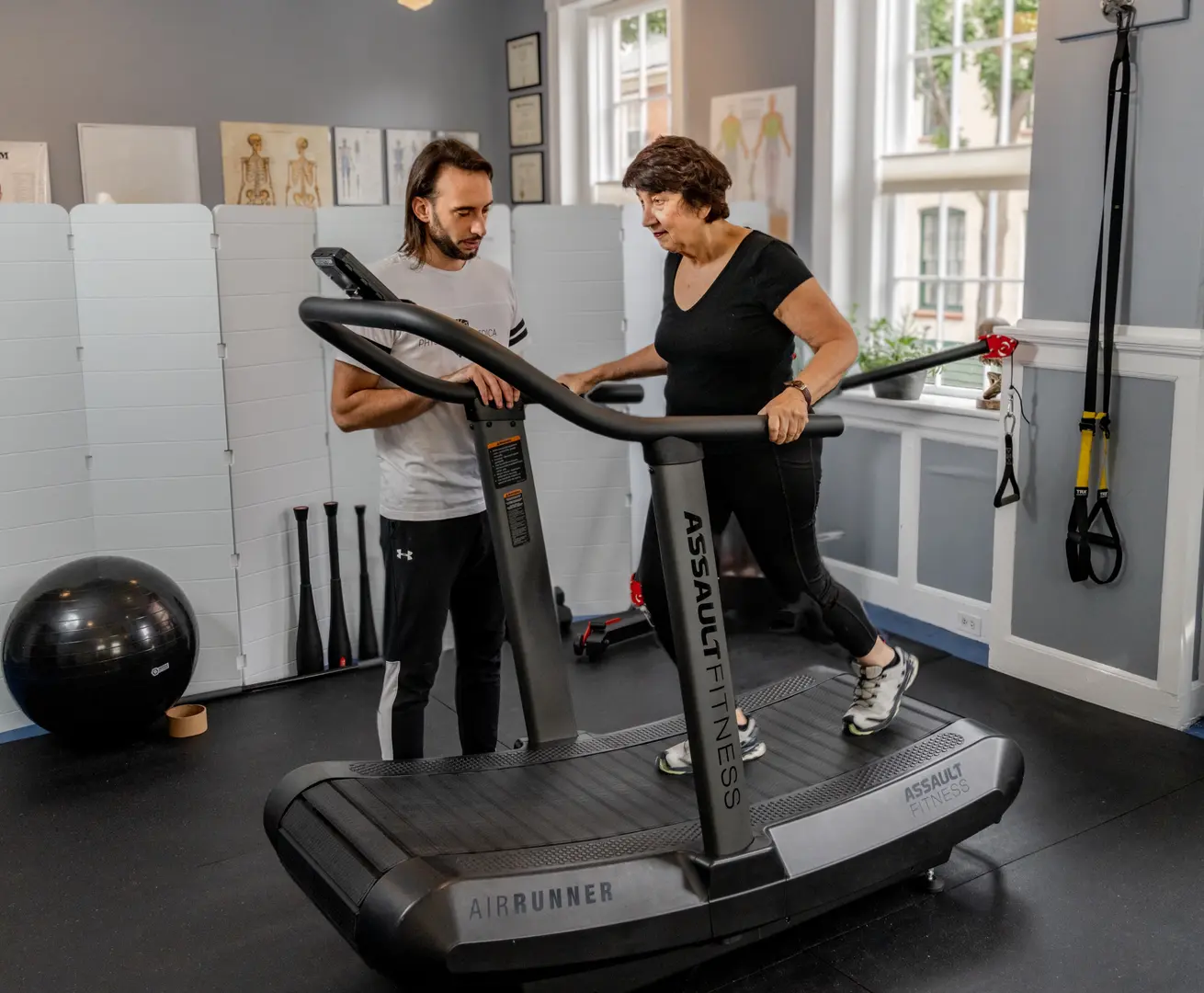 A male practitioner instructing a female client on proper form while using an air runner treadmill in a modern therapy room