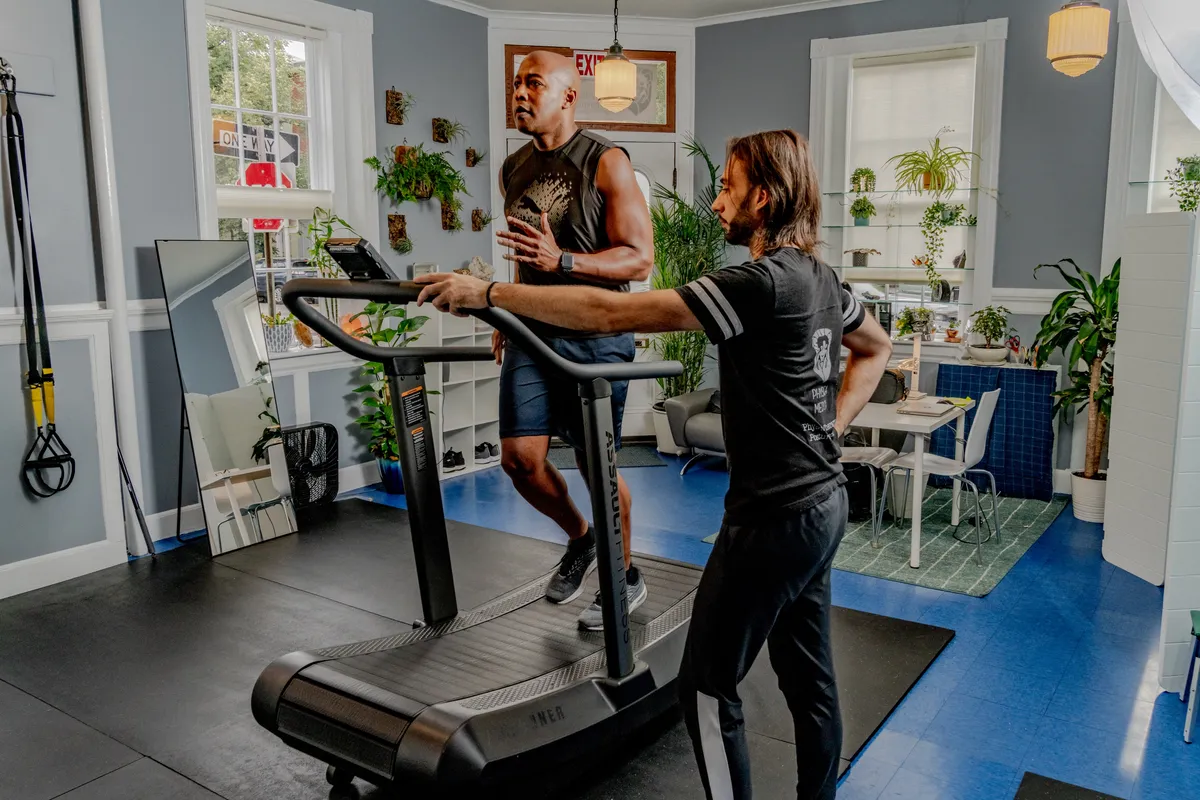 A practitioner instructing a female client on proper form while using an air runner treadmill in a bright therapy room