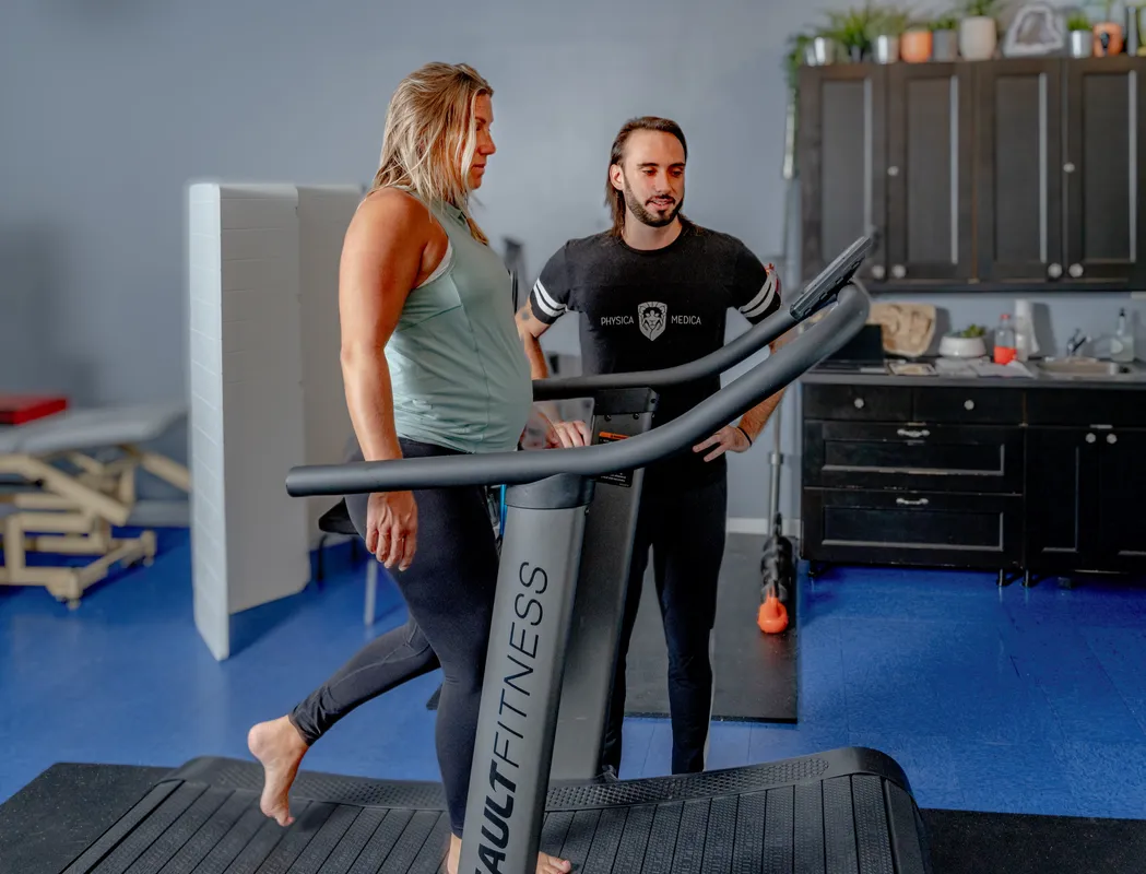 A male practitioner instructs a female client on proper form while using an exercise bike in a modern therapy facility.