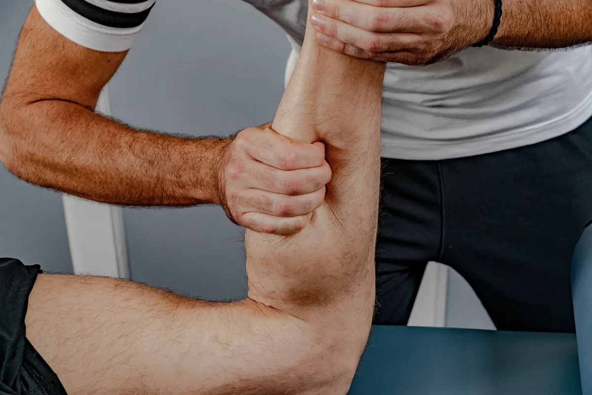 Close-up of hands demonstrating manual therapy technique on a client's arm and shoulder area.